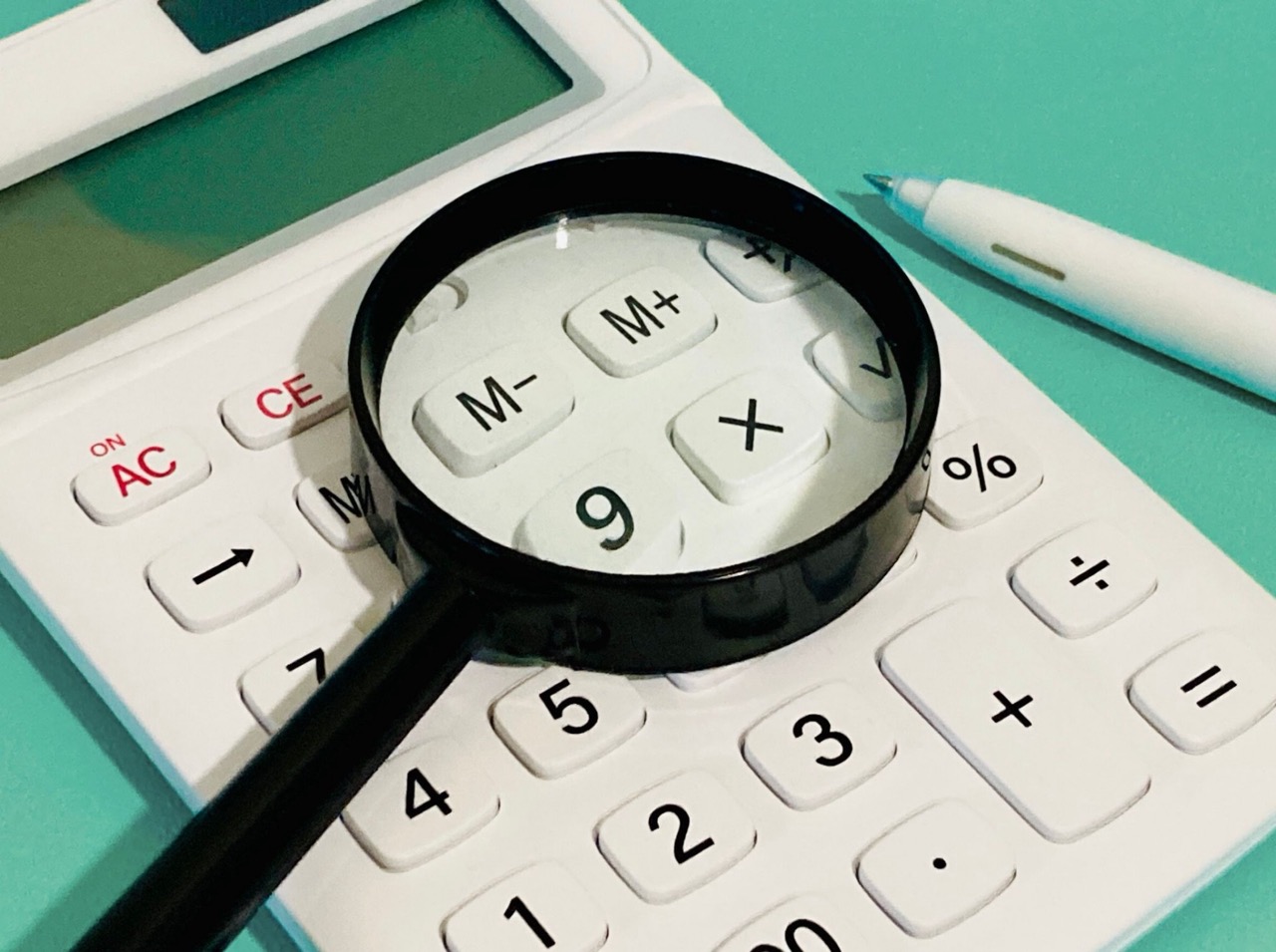 白い電卓の上に置かれた虫眼鏡とペン